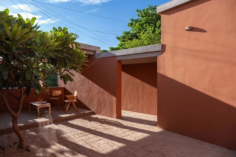 Rooftop terrace with terracotta-plastered walls and timber furniture under afternoon shadows from surrounding trees