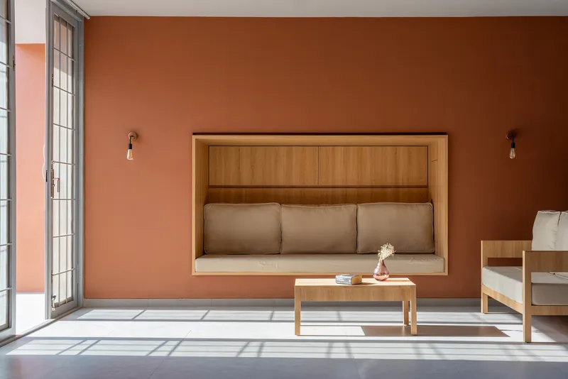 Built-in timber bench seat recessed into a terracotta wall with morning light from gridded doors
