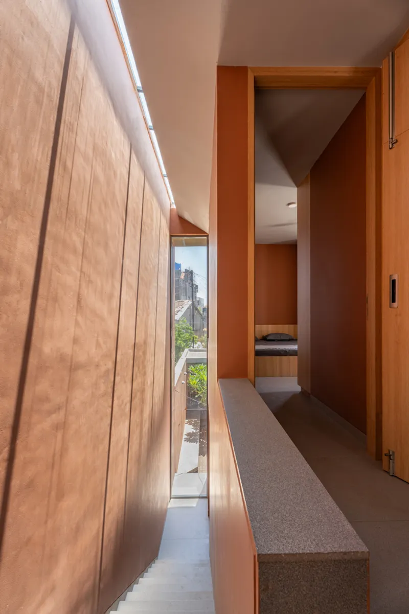 Narrow corridor with timber cabinetry and linear skylight illuminating terracotta-painted walls