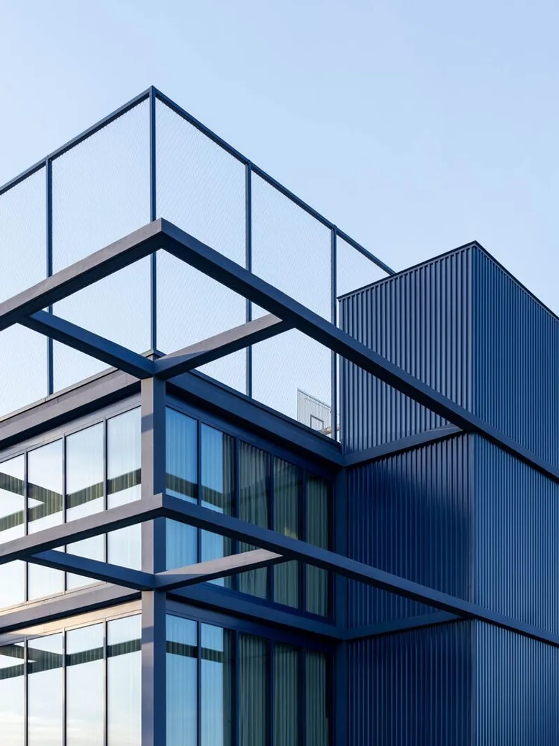 Corner detail of stacked balconies with steel frames and corrugated blue cladding against a clear sky