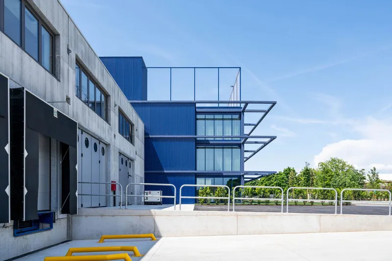 Ground-level courtyard with yellow bike racks and white bollards adjacent to cantilevered balconies and trees