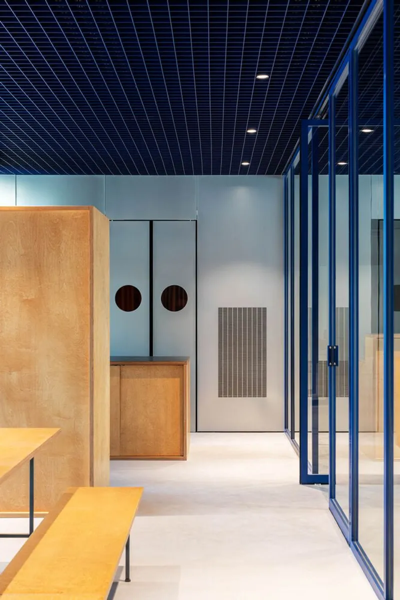 Interior corridor showing plywood casework, grey metal doors with circular portholes, and blue steel partitions