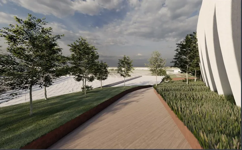 Paved pathway flanked by lawn and planted beds leading toward the stadium under a cloudy sky