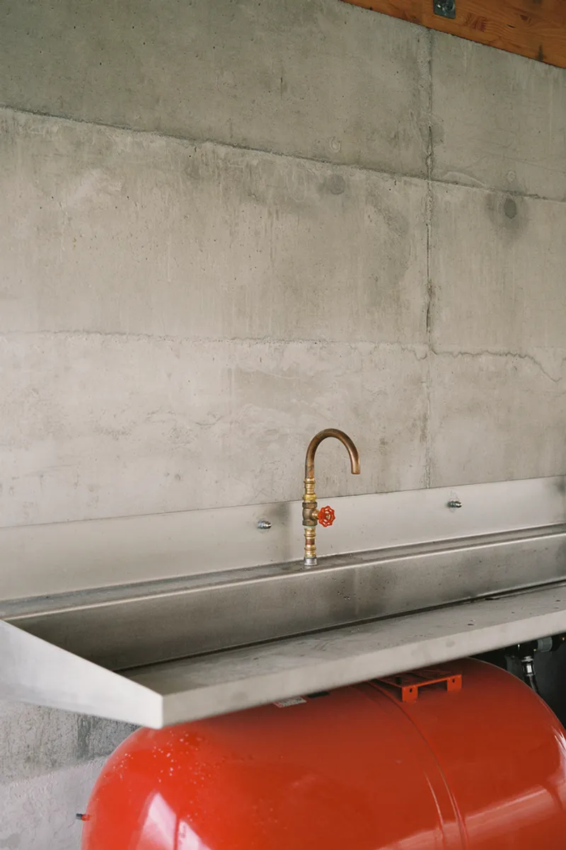 Stainless steel trough sink with copper pipe faucet mounted on board-formed concrete wall