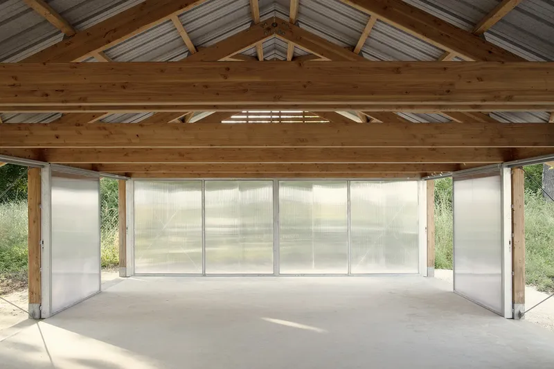 Interior with exposed timber trusses and translucent polycarbonate wall panels filtering daylight