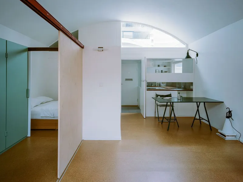 Open-plan interior showing kitchen counter, plywood partition and arched window with natural light