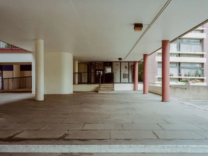 Covered terrace with cylindrical columns in cream and pink beneath an overhanging concrete soffit