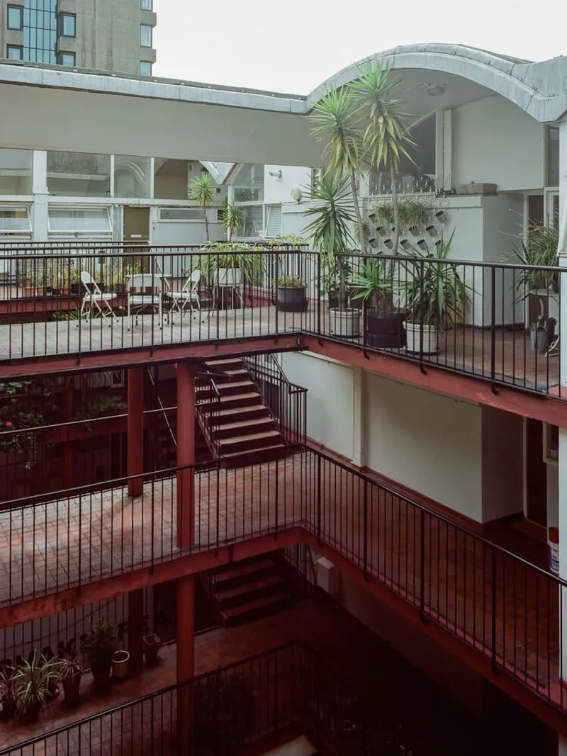 Interior courtyard with red painted steel staircase, balconies and potted palms under diffused daylight