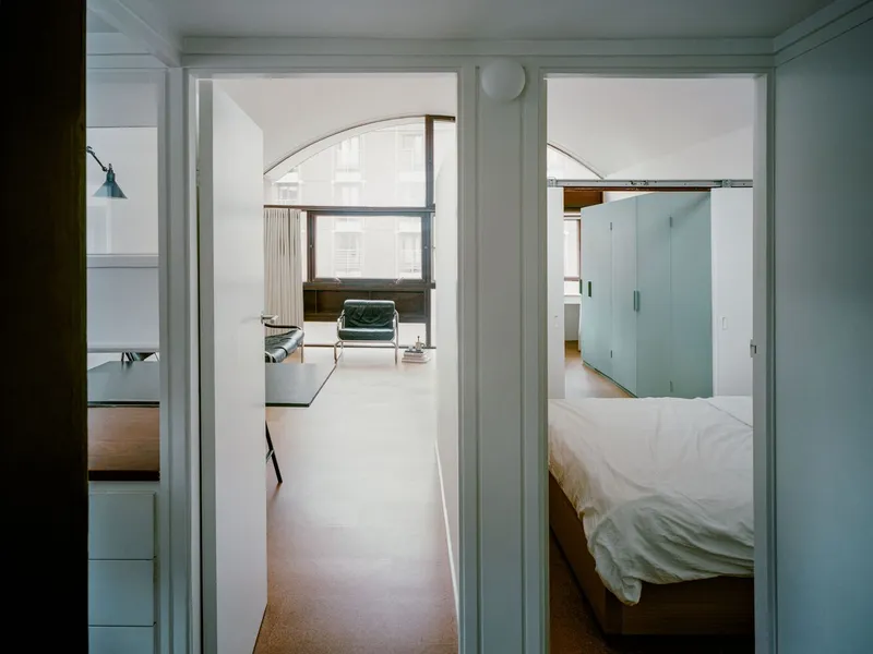 View through arched doorways linking pale green bedroom and living space in overcast daylight