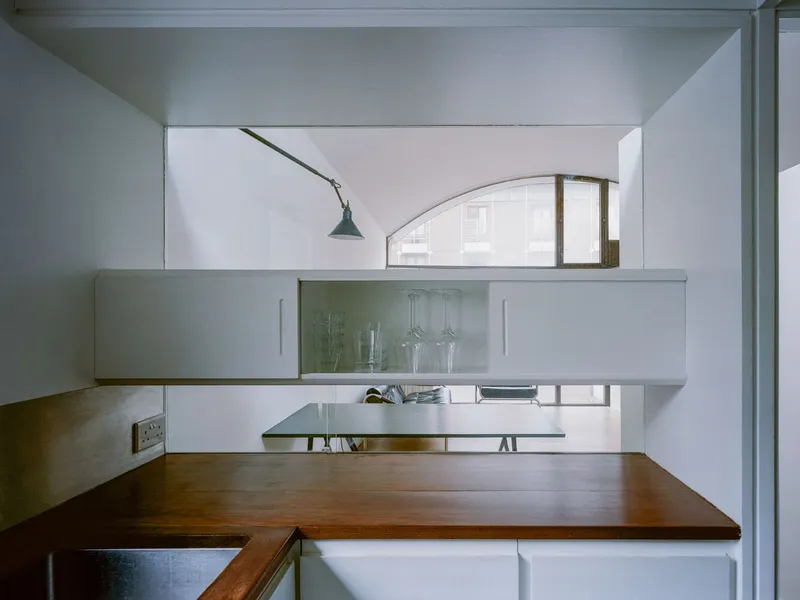 Kitchen counter with timber worktop and pale green cabinetry beneath an articulated wall lamp