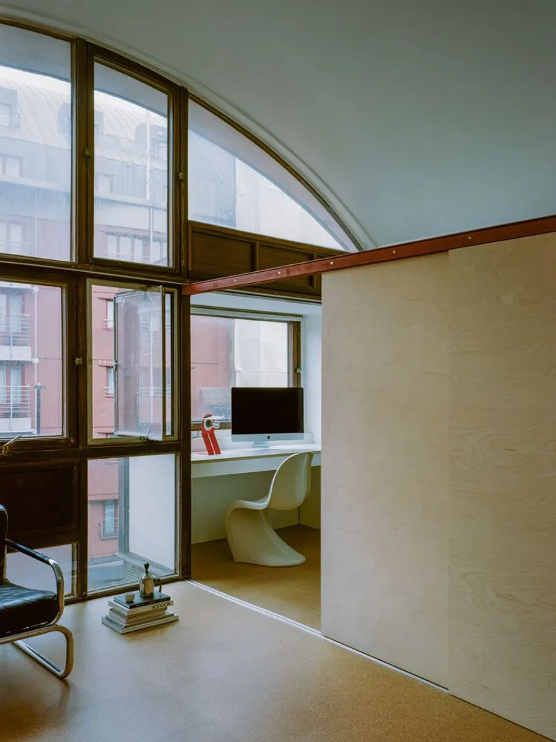 Arched window wall with timber frames overlooking adjacent buildings and a sliding plywood partition