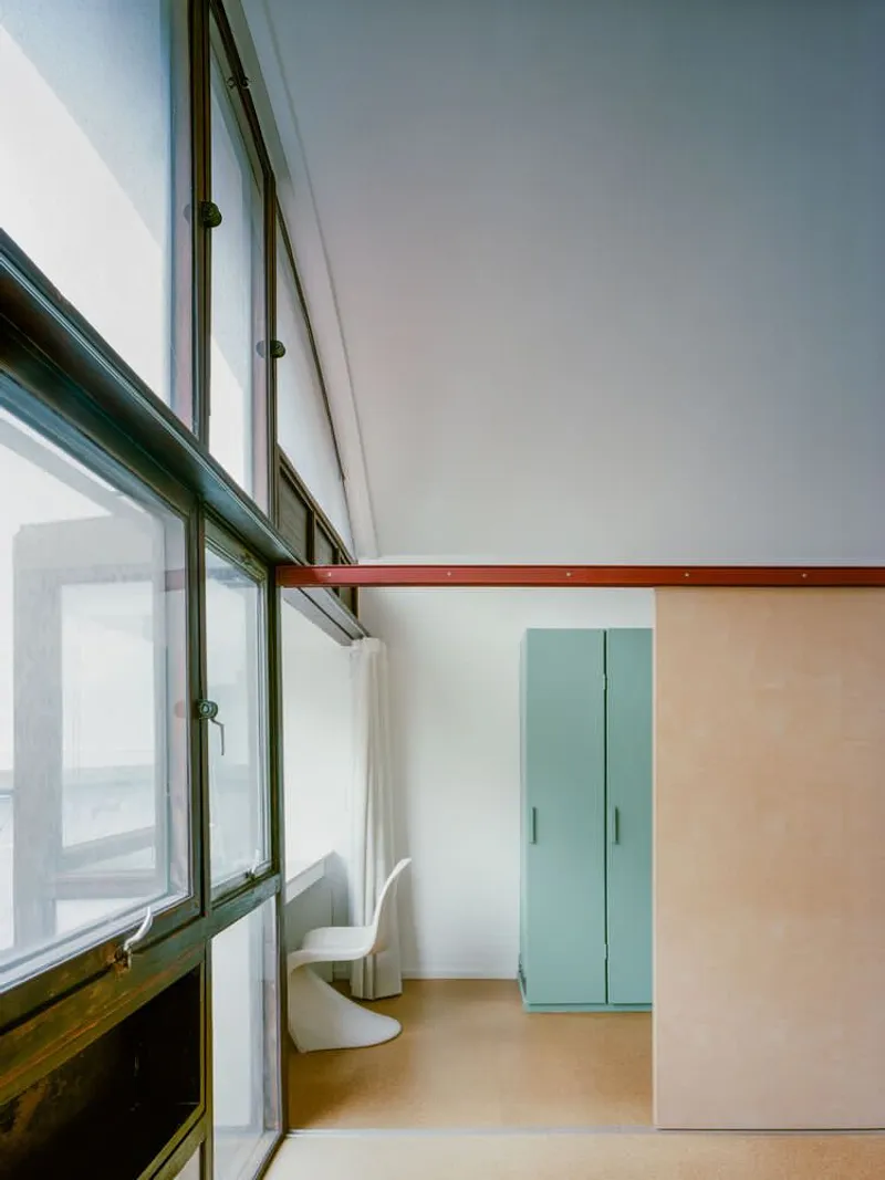 Interior corner showing arched glazing with timber beam and pale green storage cabinets in soft light