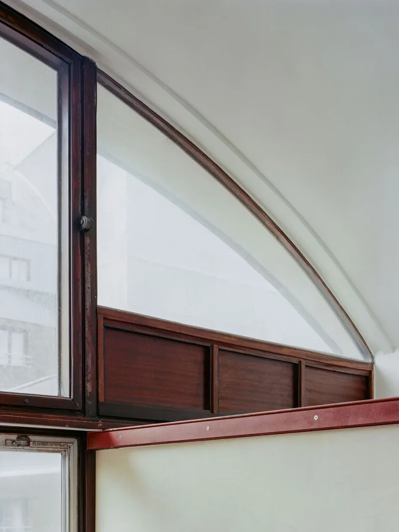 Close-up of arched window detail with timber frame and paneled infill meeting painted wall