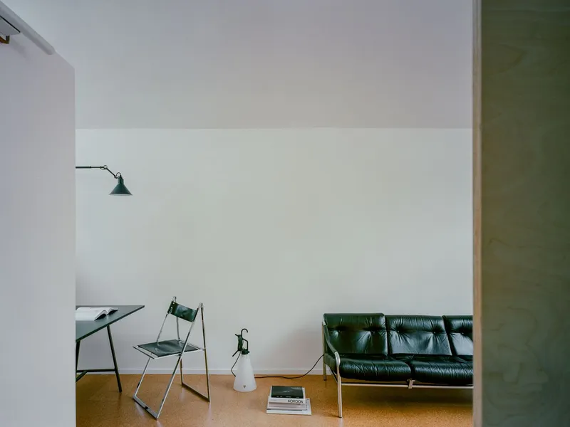 White interior corner with cork flooring, black leather sofa and articulated wall lamp