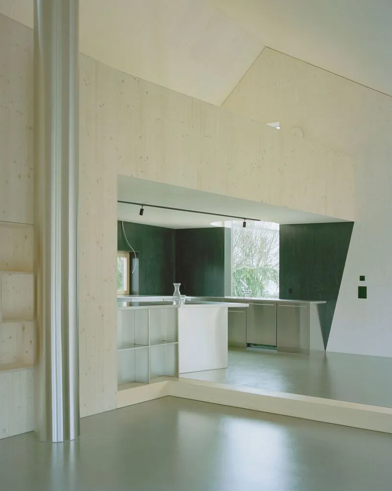 View through doorway to kitchen with green tiled backsplash and white island under plywood vaulted ceiling