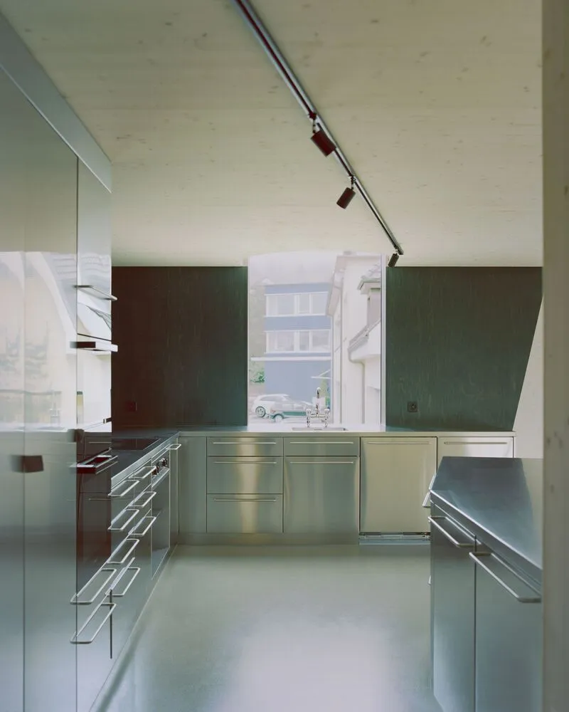 Kitchen with stainless steel cabinetry and angled dark wood range hood under pale wood ceiling