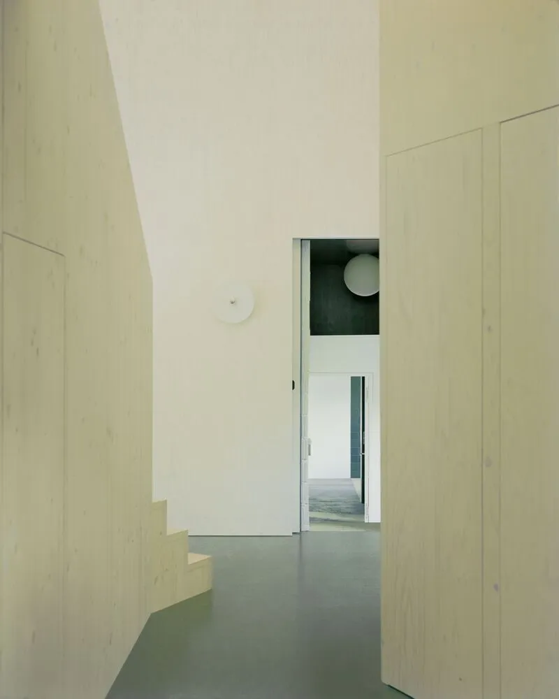 Interior hallway with pale wood staircase and doorway framing views through multiple rooms
