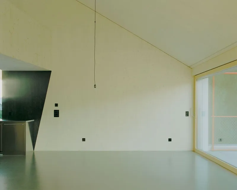 Interior room with pale plywood walls and angled doorway opening to green tiled bathroom