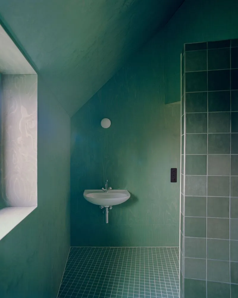 Green tiled bathroom with wall-mounted sink and glazed shower enclosure under the sloped ceiling