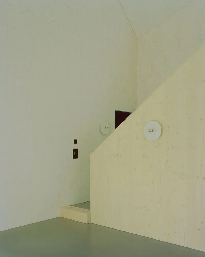 Plywood partition wall with circular light fixture and dark threshold opening beneath the gable