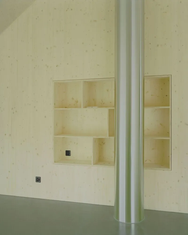Recessed plywood shelving niches in pale wood paneling with a white-painted column and grey resin floor