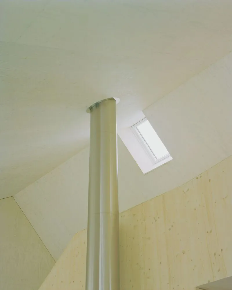 Skylight window set into sloped pale plywood ceiling with a white cylindrical column passing through
