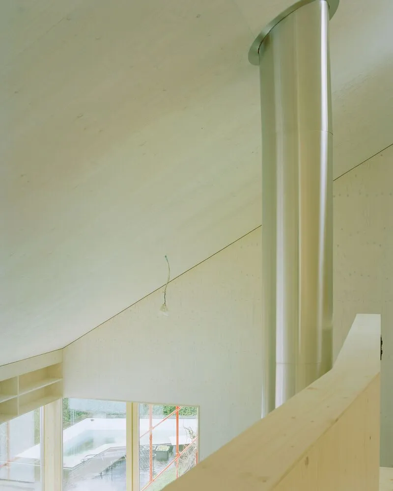 Double-height interior space with pale plywood cladding and a white column alongside upper windows