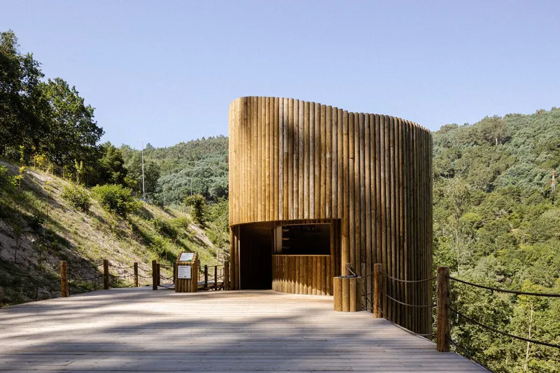 Cylindrical timber pavilion with vertical slat cladding and recessed entrance on a concrete platform