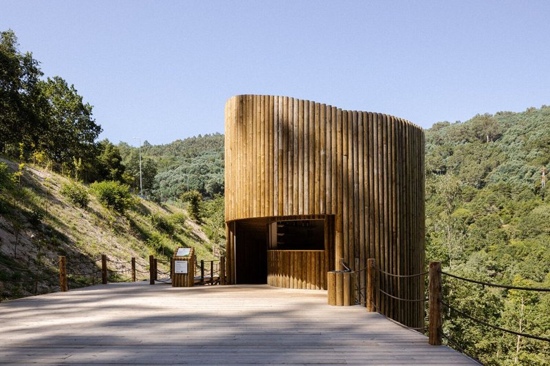 Cylindrical timber pavilion with vertical slat cladding and recessed entrance on a concrete platform