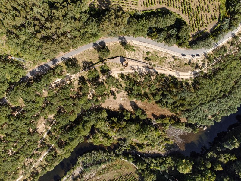 Aerial view of curved paths and cylindrical structure nestled in forested valley near vineyards