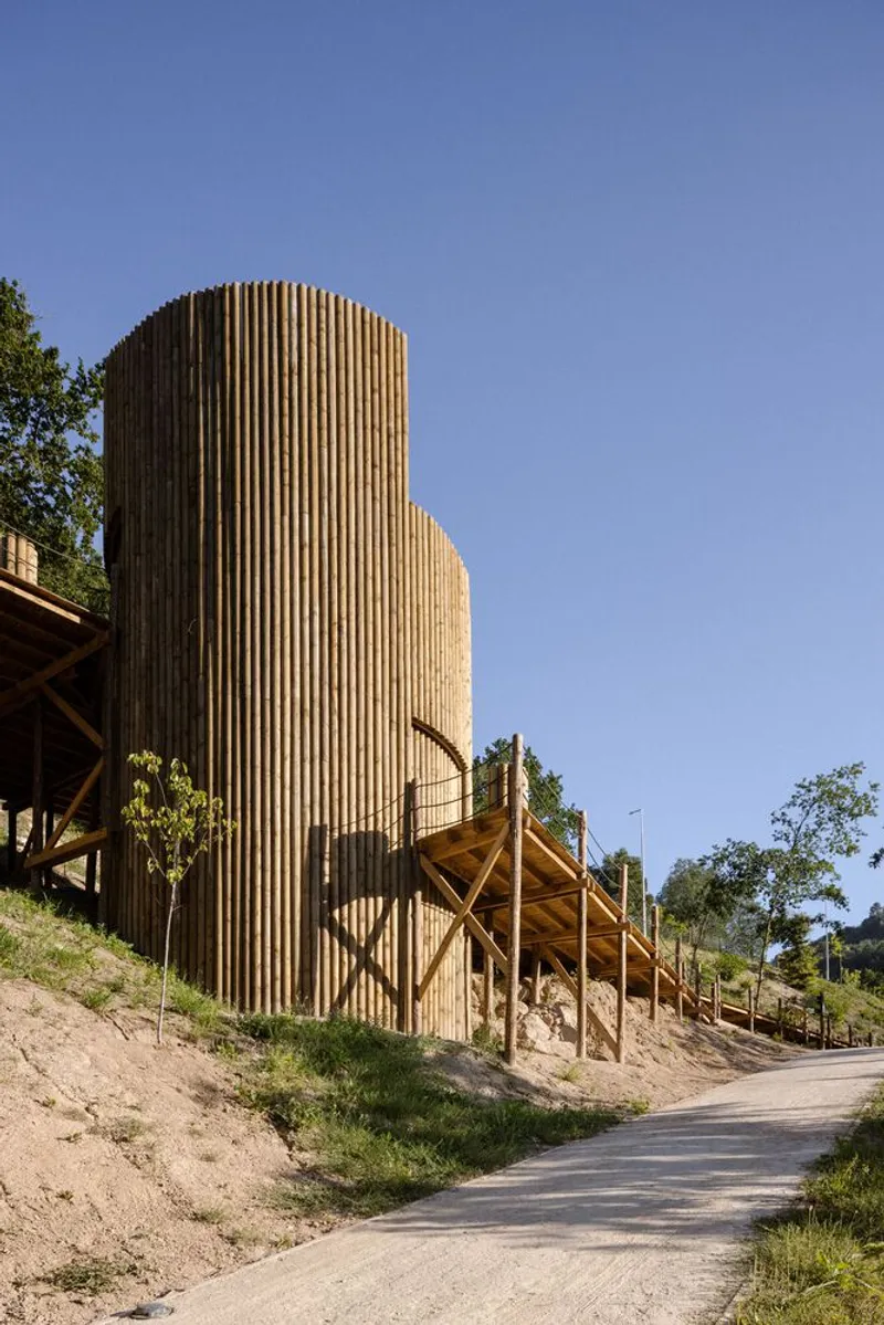 Rounded timber-slatted tower rising above timber walkway with young trees dotting the hillside