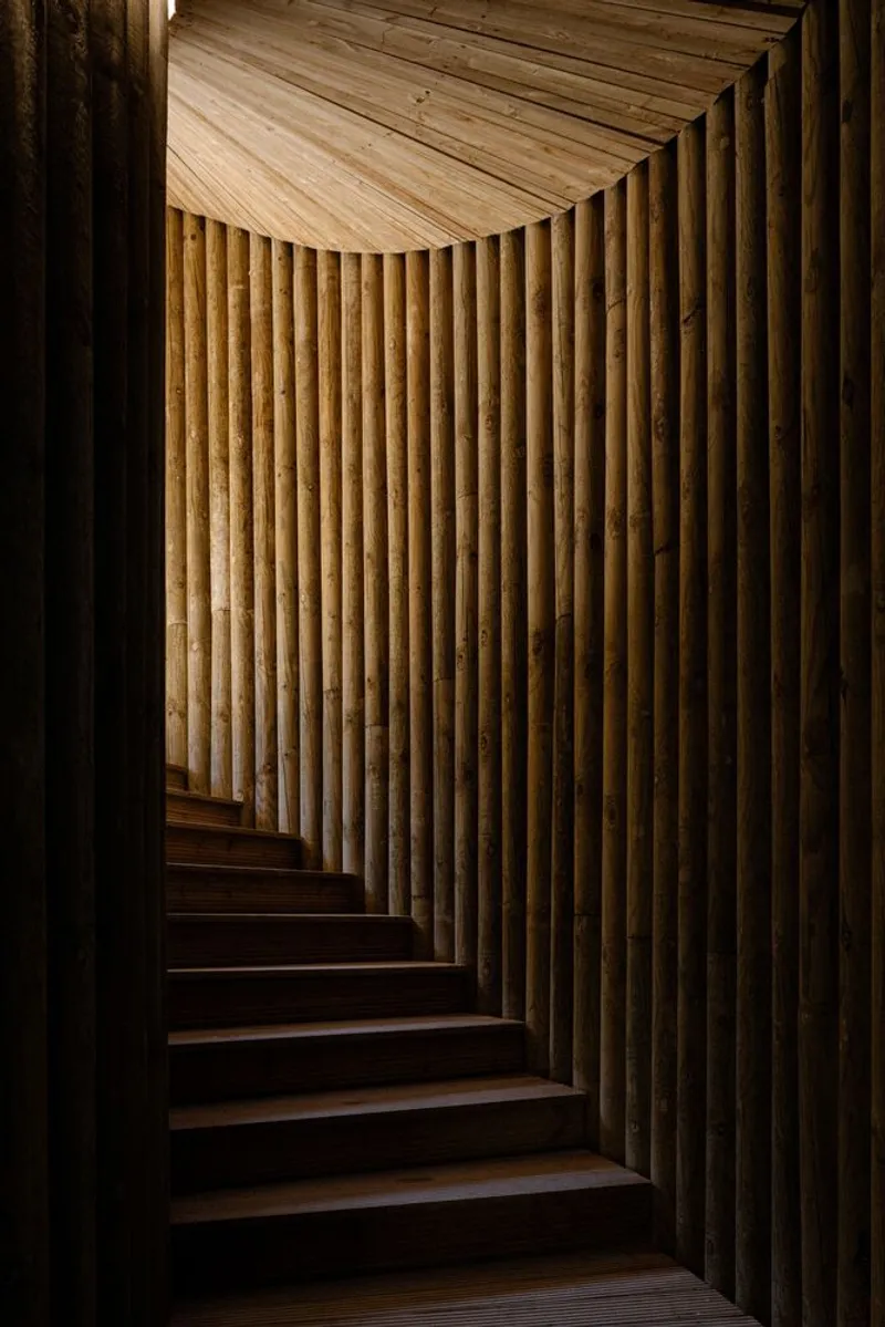 Interior staircase winding upward with vertical timber slats and slatted ceiling lit from above