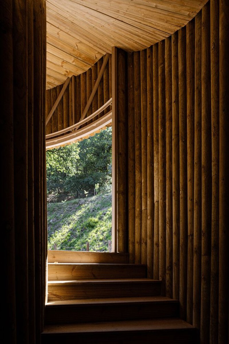 Timber staircase framed by vertical wood slats with opening to green hillside beyond