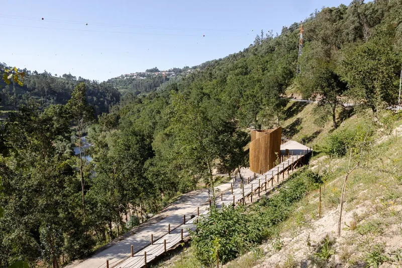 Elevated timber walkway with handrails leading to wood-clad structure on forested hillside