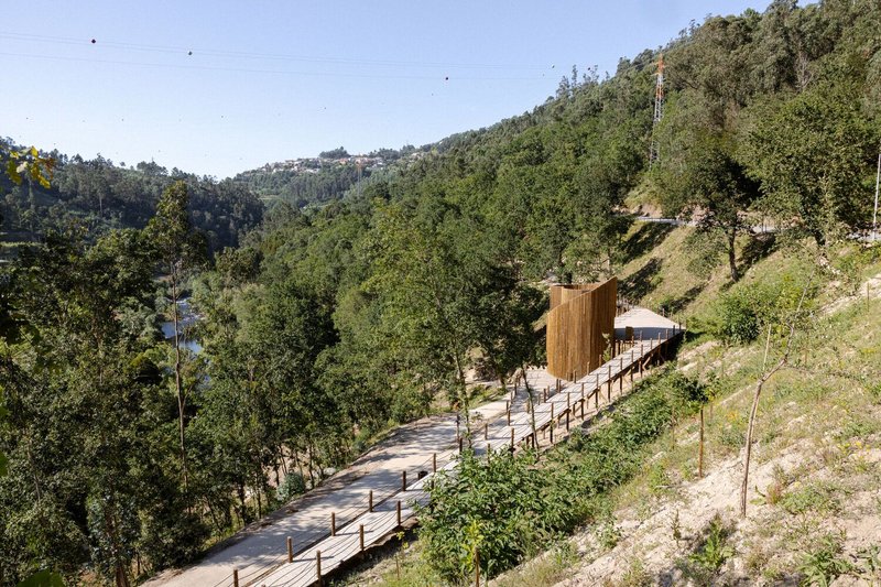 Elevated timber walkway with handrails leading to wood-clad structure on forested hillside