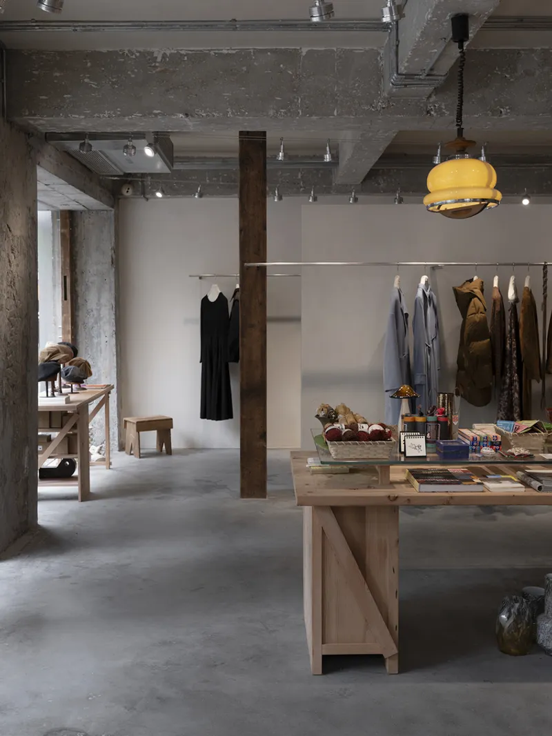 Interior retail space with exposed concrete columns and ceiling alongside timber display tables and hanging garments