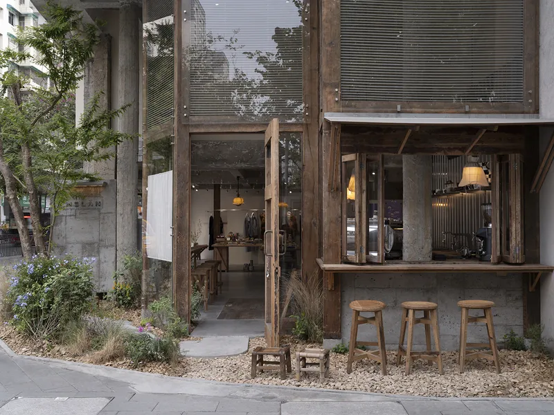 Exterior timber bar counter with stools opening onto a gravel garden bed with shrubs and grasses