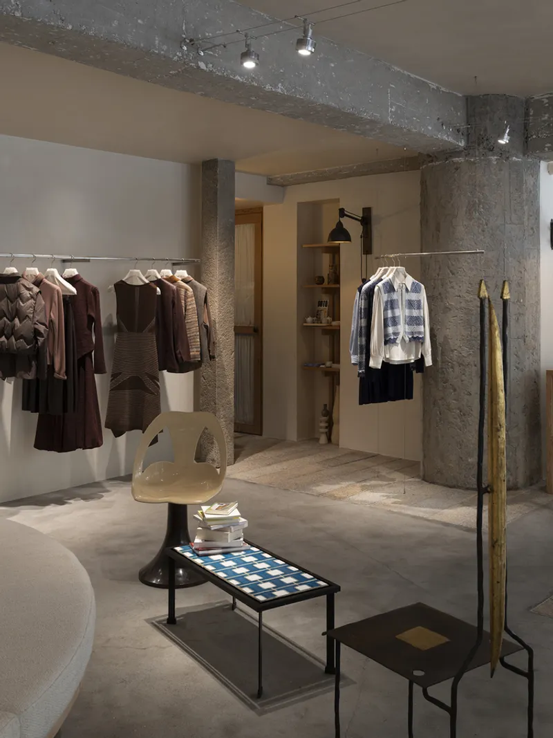 Retail interior with raw concrete columns and exposed ceiling beams framing suspended clothing racks
