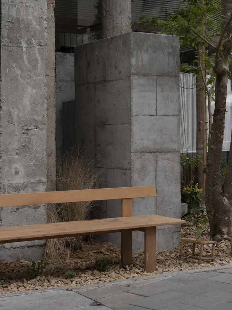 Timber bench in front of board-formed concrete wall with gravel ground cover and plantings