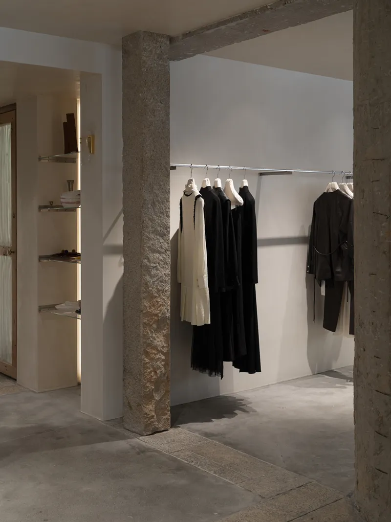 View through concrete columns toward a clothing rail under warm directional lighting at dusk