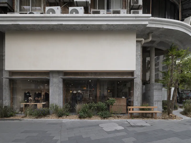 Street facade with exposed concrete frame, recessed glazing, and planted beds with wooden bench