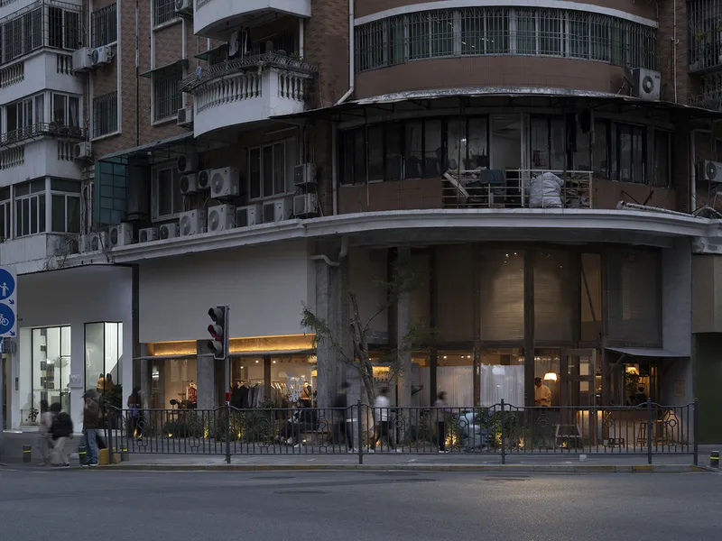 Curved corner storefront with glass facade and pedestrians passing along the sidewalk at dusk