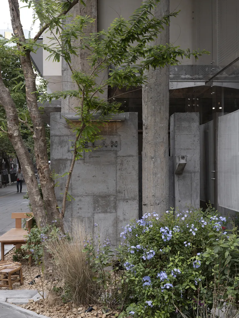 Concrete column beside planted bed with blue flowering plants and young tree