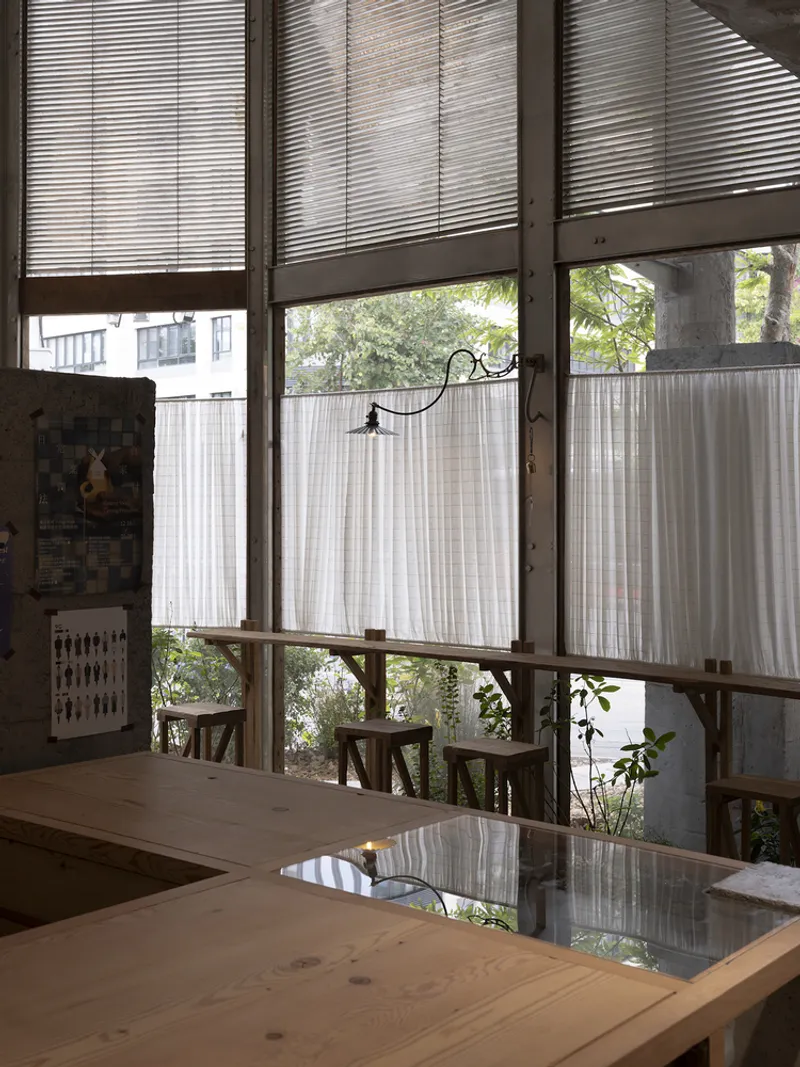 Timber table with glass insert beneath tall windows with half-height curtains and blinds