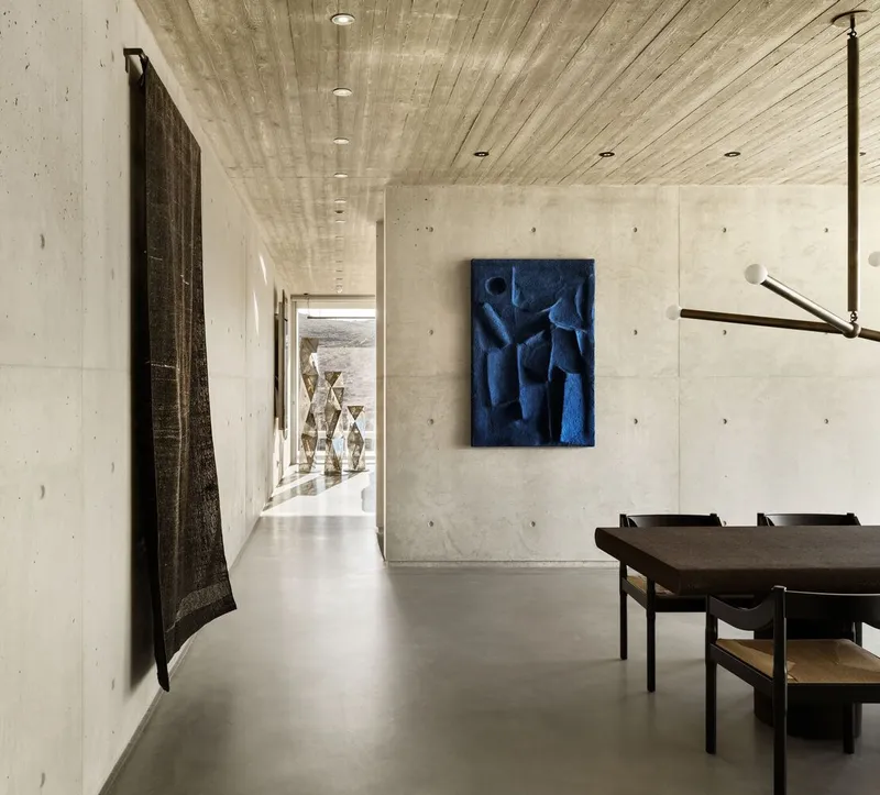 Dining area with board-formed concrete walls and ribbed timber ceiling under natural light from the corridor