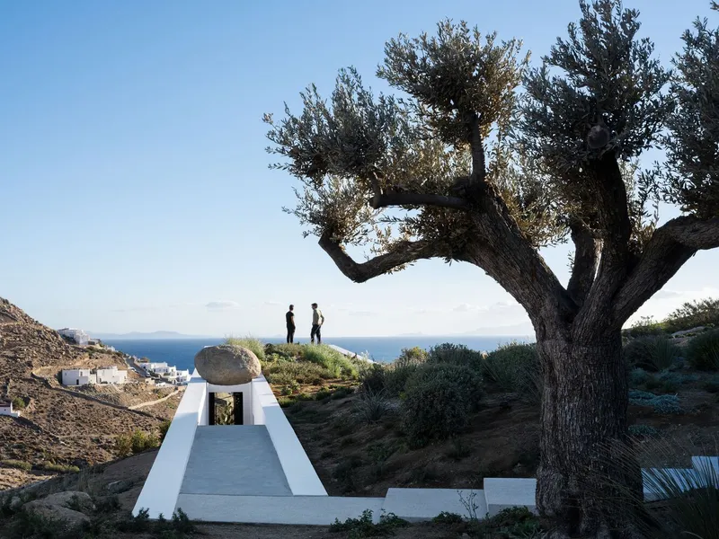 Approach stair flanked by white walls leading to a boulder under an old olive tree