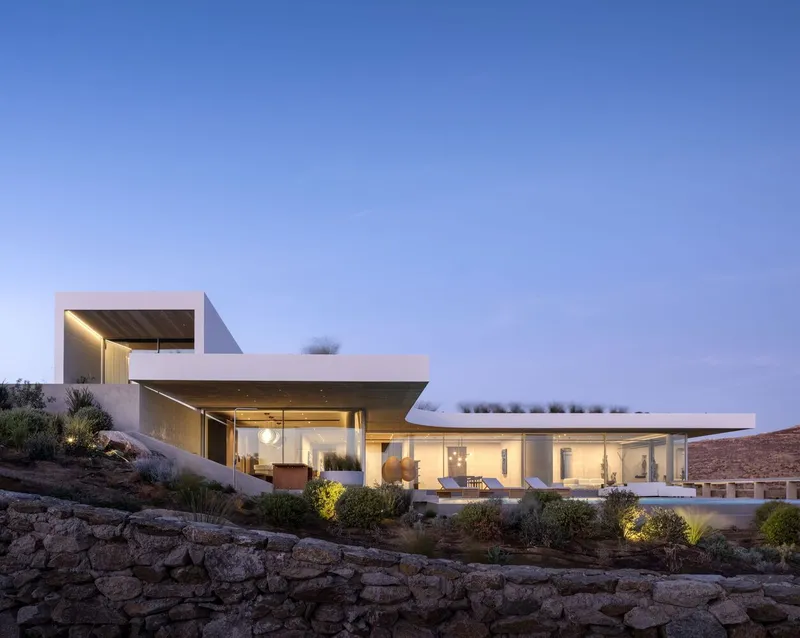 Exterior view of the white cantilevered volumes on a terraced stone base at dusk