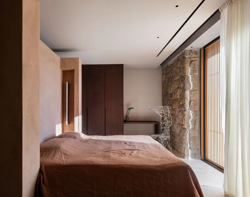 Bedroom with exposed stone wall, dark timber cabinetry and recessed linear ceiling light