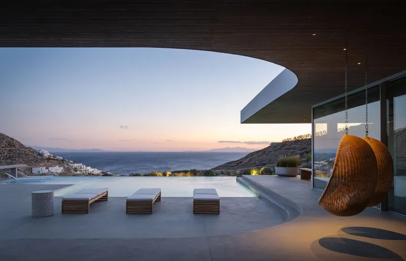 Poolside terrace with woven hanging chair and curved roof overhang at dusk