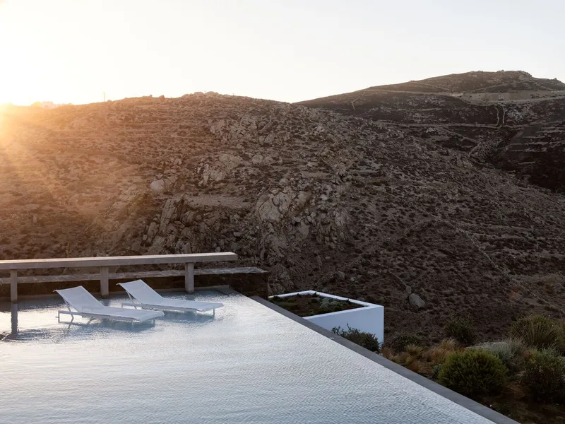 White loungers on pool deck facing rocky hillside in bright morning sunlight